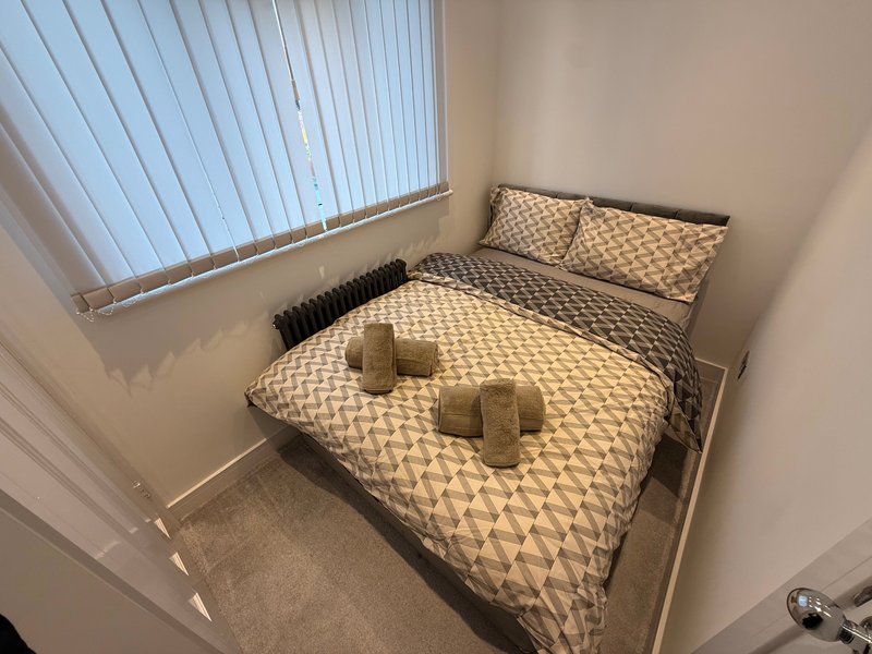 Bedroom with double bed, geometric patterned bedding, pillows, and vertical blinds