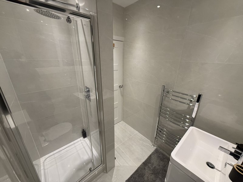 Modern bathroom with shower cubicle, towel radiator, white sink and tiled walls