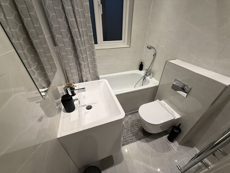 Modern bathroom with white sink, toilet, bathtub and grey shower curtain