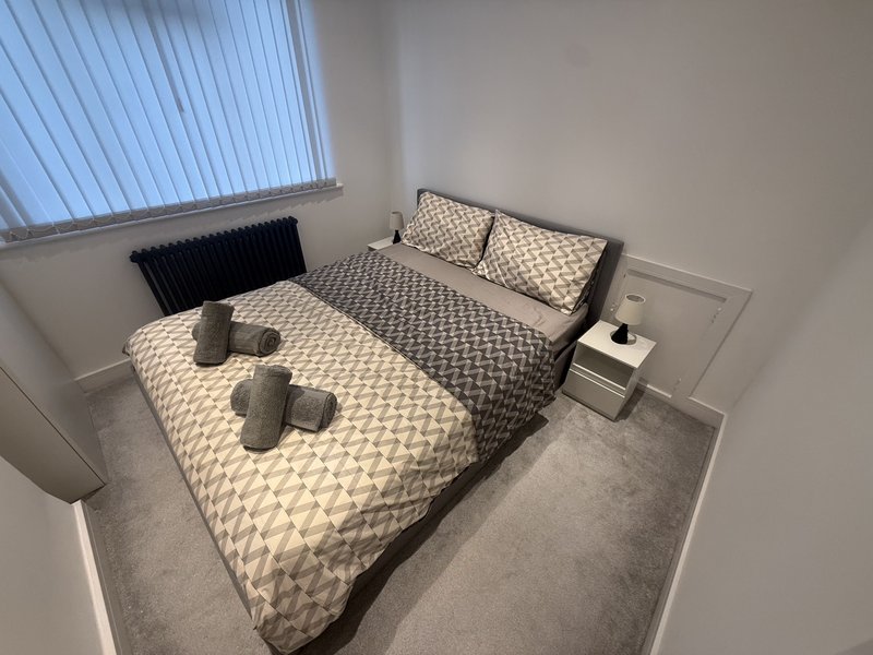 Bedroom with double bed, patterned bedding, pillows, and bedside table by window