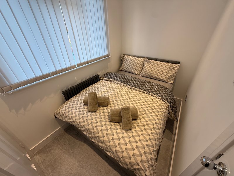 Bedroom with double bed, patterned bedding, pillows, and vertical blinds on window