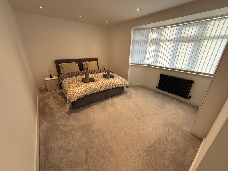 Spacious bedroom with double bed, beige carpet, large window and radiator