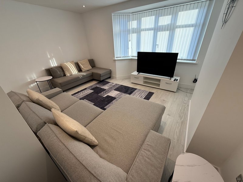 Modern living room with grey sofas, TV stand, patterned rug and vertical blinds
