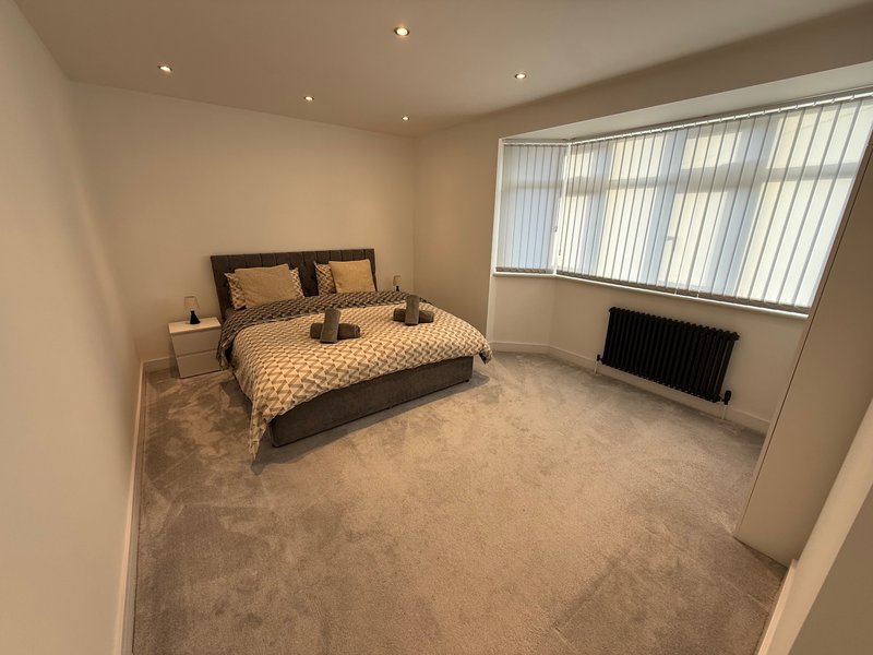 Spacious bedroom with double bed, bedside tables, radiator and vertical blinds
