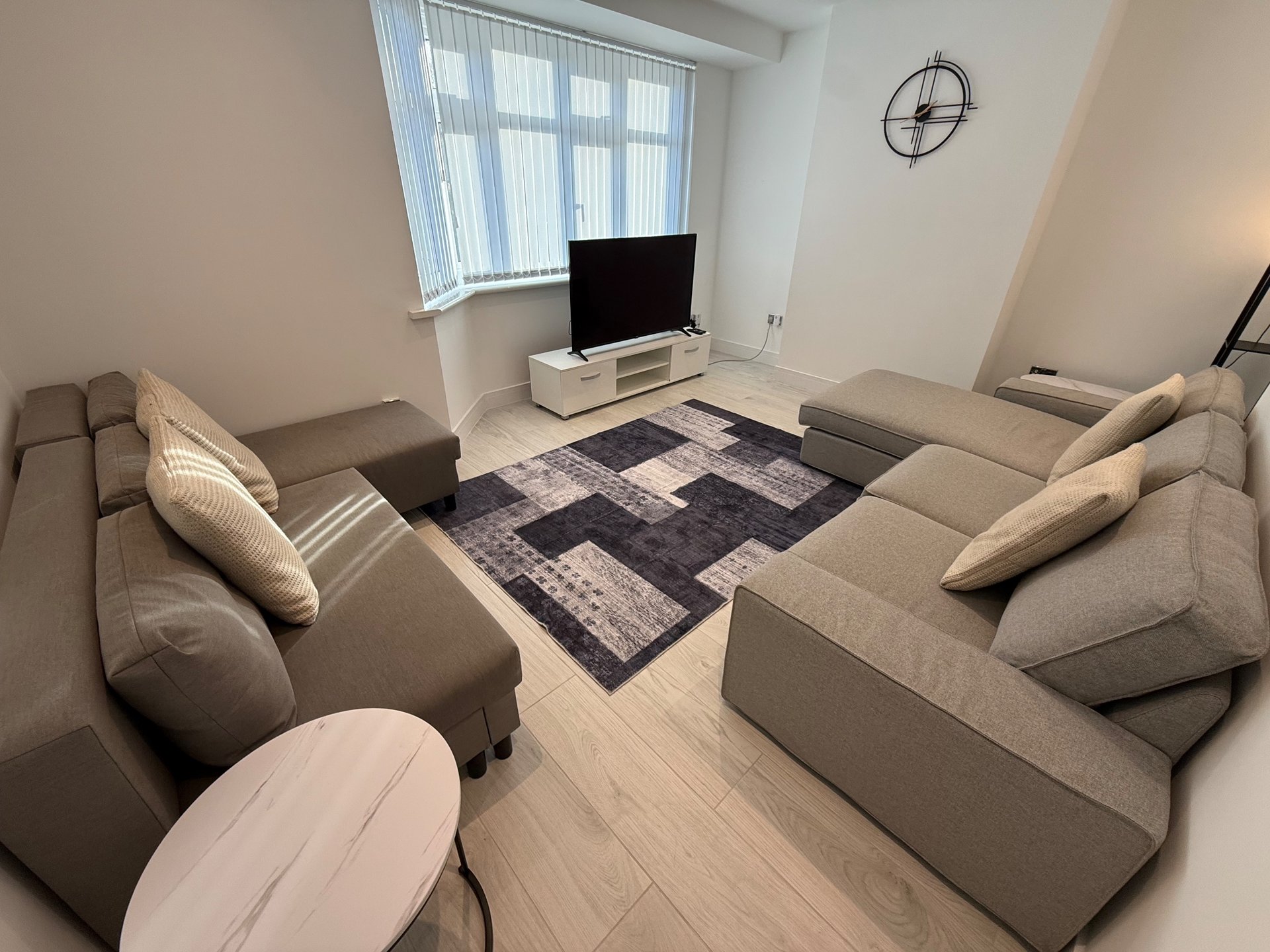 Modern living room with two beige sofas, TV stand, geometric area rug, and wall clock
