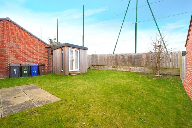 Spacious back garden with green lawn, wooden garden shed, waste bins and swing frame