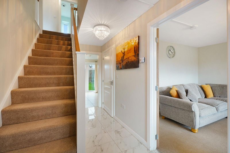 Hallway with carpeted staircase, chandelier, abstract wall art, and glimpse of sofa in adjacent room