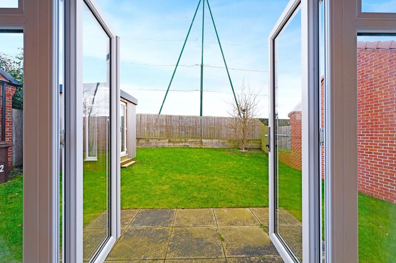 View through open patio doors to garden with lawn, paving, and fencing