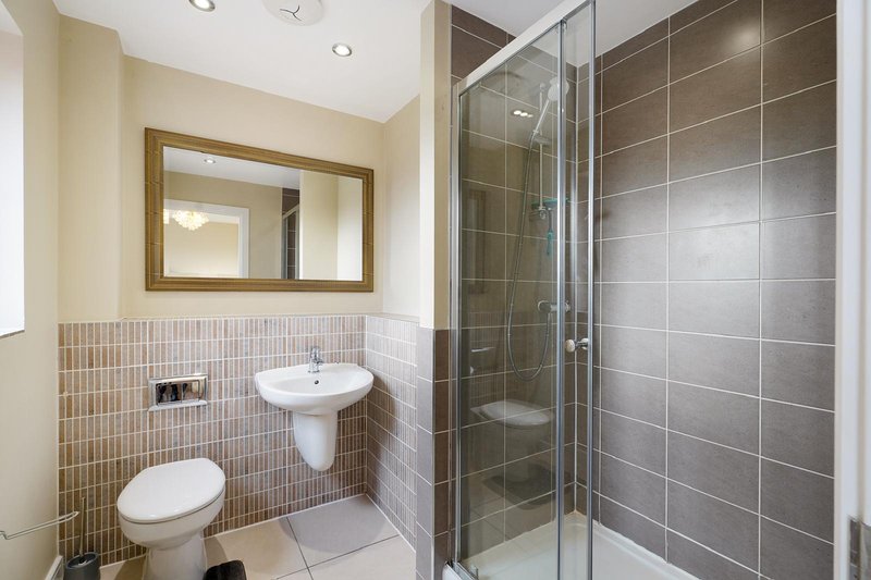Modern bathroom with toilet, pedestal sink, mirror, and enclosed shower cubicle with gray tiles