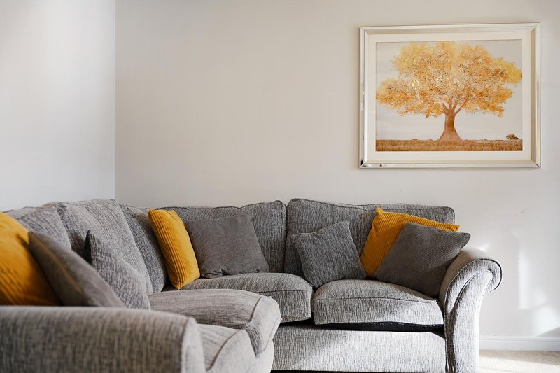 Grey upholstered sofa with yellow and grey cushions beneath framed tree artwork