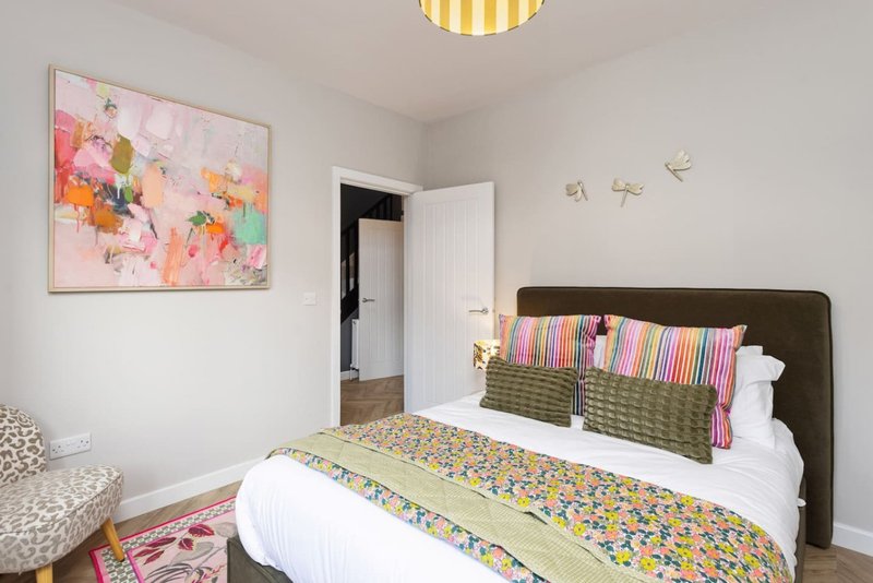 Bright bedroom with double bed, colorful bedding, framed floral artwork, and yellow ceiling light