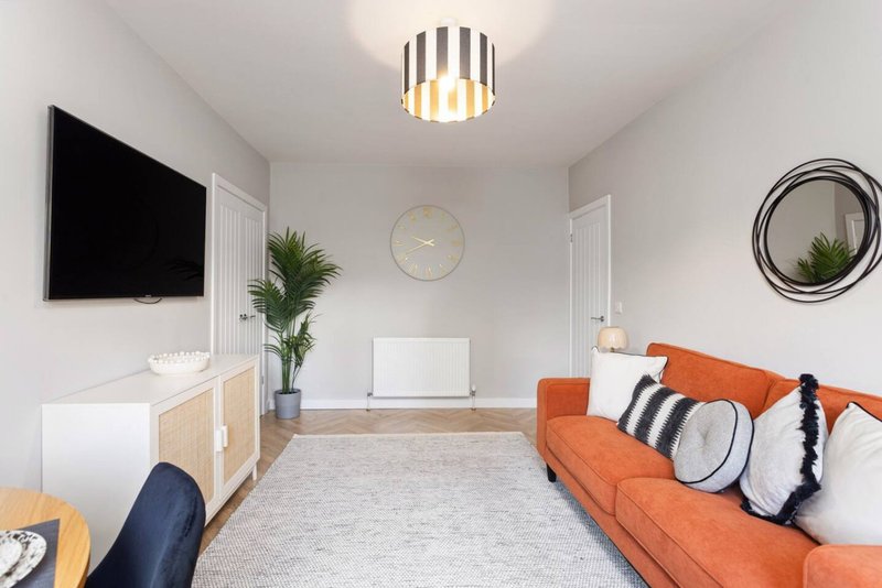 Modern living room with orange sofa, TV, plant, round mirror and striped ceiling light