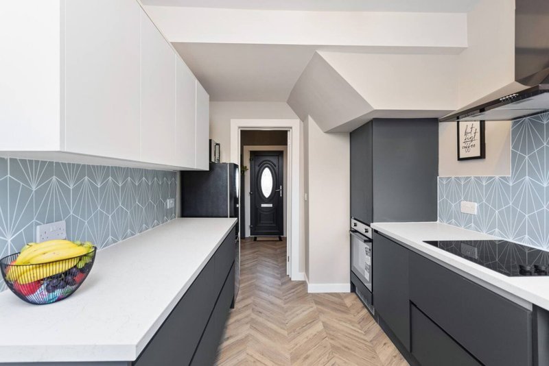 Modern galley kitchen with white and dark cabinetry, herringbone flooring, and geometric backtile