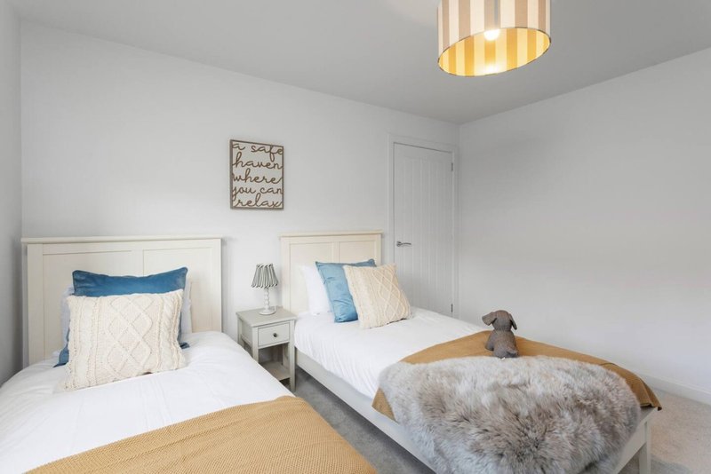 Bright bedroom with two single beds, white headboards, blue and cream pillows, wooden nightstand, and striped ceiling light.
