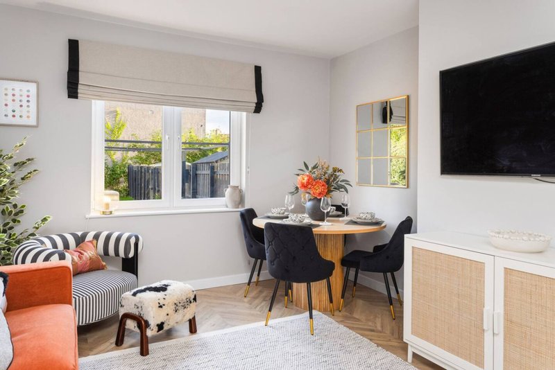 Bright living room with dining table, black chairs, TV, and window seating area with orange accents