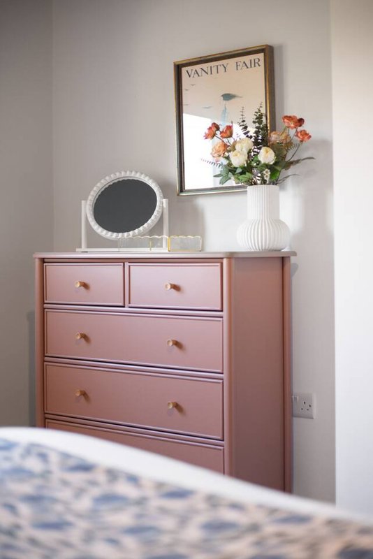 Pink dresser with mirror, flowers, and Vanity Fair magazine cover framed on wall