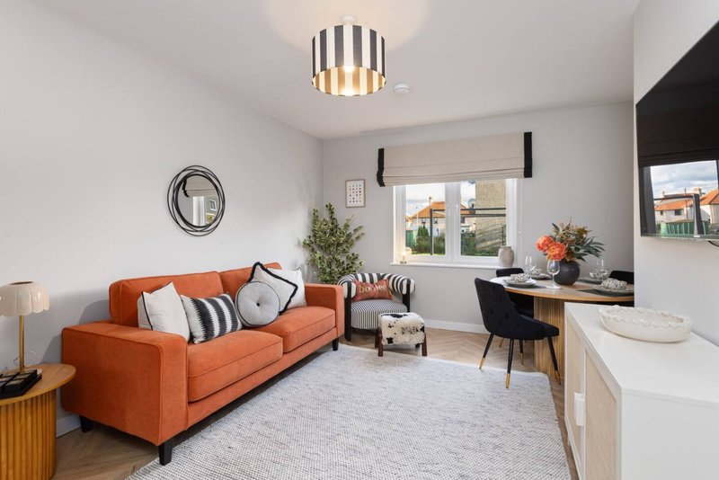 Modern living room with orange sofa, striped ceiling light, desk area and kitchenette