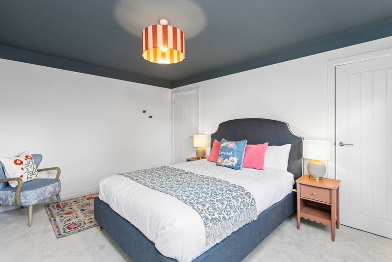 Bright modern bedroom with dark blue bed, colorful pillows, wooden nightstands and striped ceiling light