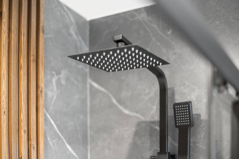 Modern bathroom shower head and hand spray mounted on grey tiled wall