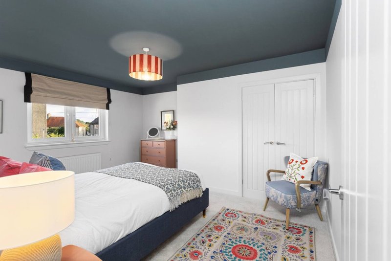Modern bedroom with double bed, white wardrobes, patterned rug and upholstered armchair