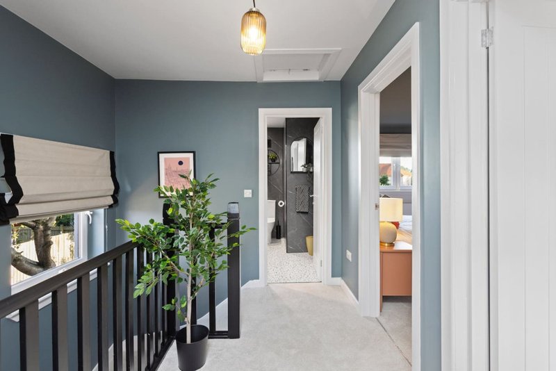 Modern hallway with blue-grey walls, pendant light, staircase railing, potted plant and open doorways