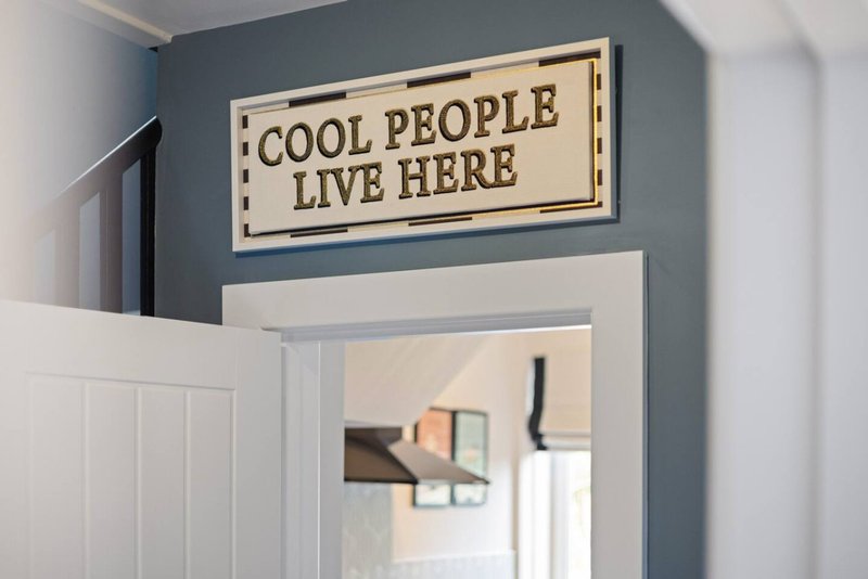 Hallway with blue-gray walls, white door frame, and wooden wall sign reading Cool People Live Here