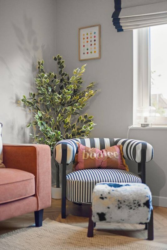 Living room corner with pink armchair, striped upholstered chair, potted plant and window
