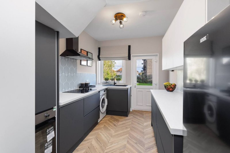 Modern kitchen with dark cabinetry, white countertops, integrated appliances and garden view