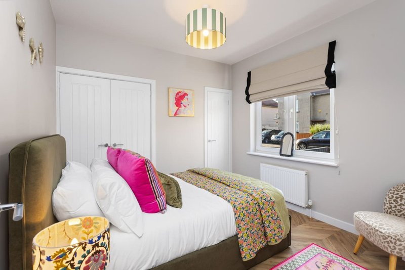 Bright bedroom with double bed, colorful pillows and throw, window with black curtain pole, ceiling light fixture