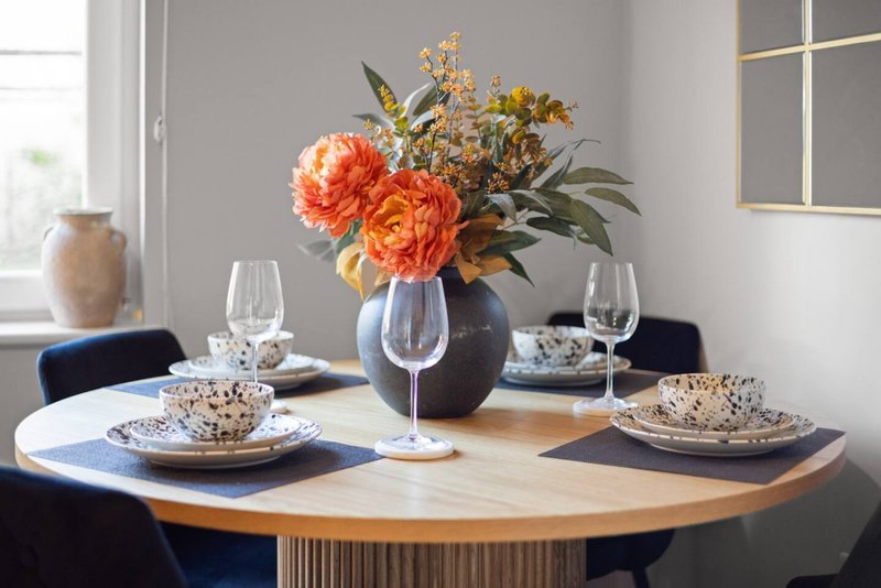 Dining table with floral centerpiece, place settings, and glasses by window