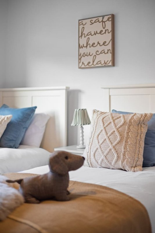 Bedroom with twin beds, blue and pink pillows, decorative wall sign, and stuffed dog toy