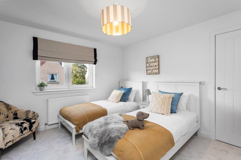 Bright bedroom with two white beds, gold throws, blue pillows, and striped ceiling lamp
