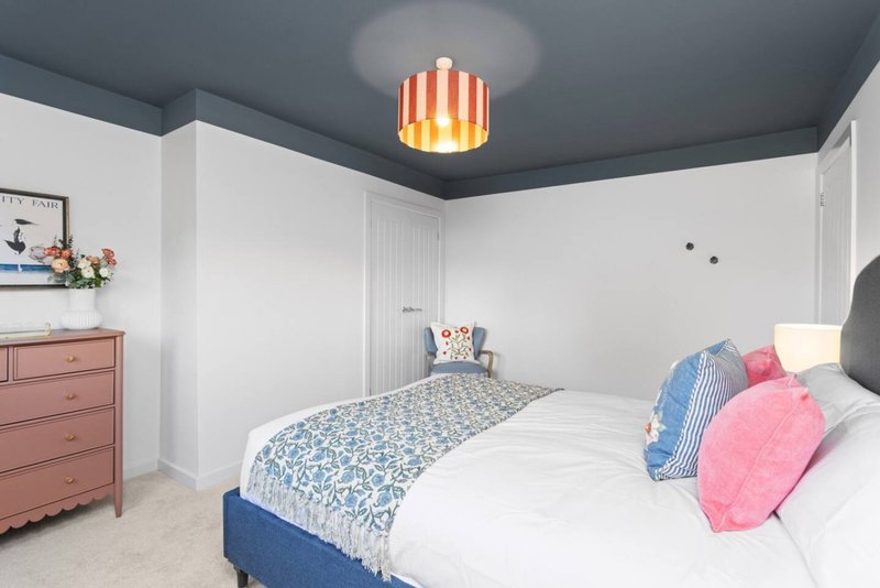 Bright bedroom with double bed, blue headboard, pink and blue cushions, wooden dresser, pendant light