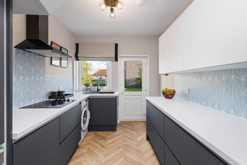 Modern kitchen with dark cabinetry, white countertops, washing machine, and patterned tile backsplash