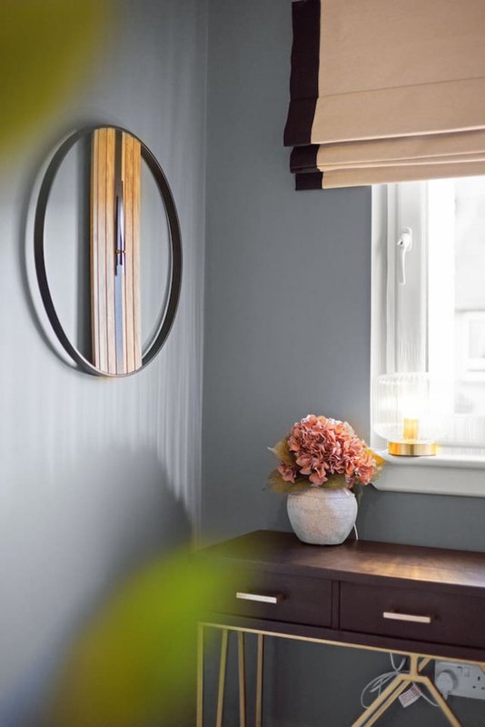 Bedroom corner with oval mirror, dark desk, potted flowers, and window with blinds