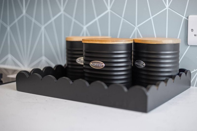 Kitchen counter styling with three black cylindrical containers with wooden lids and branded labels