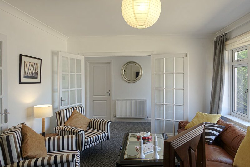 Bright living room with striped armchairs, leather sofa, coffee table, and large windows