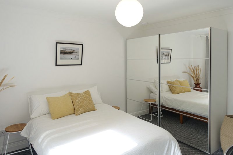 Bright bedroom with white bed, yellow cushions, mirrored wardrobe and framed wall art