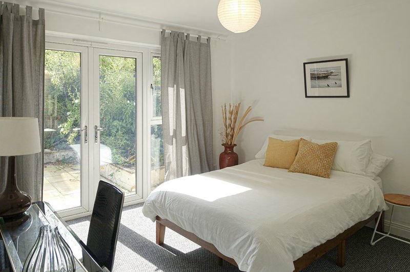 Bright bedroom with double bed, yellow cushions, glass doors to garden, desk and pendant light