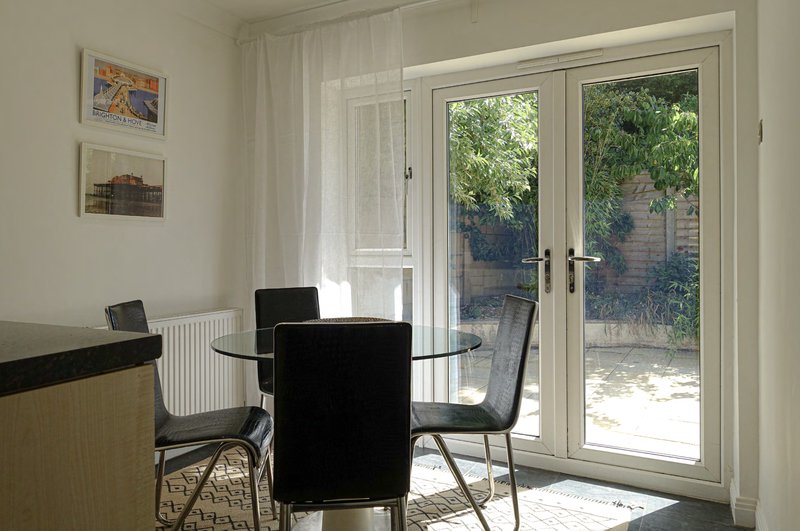 Bright dining area with round black table, two chairs, glass doors opening to garden patio