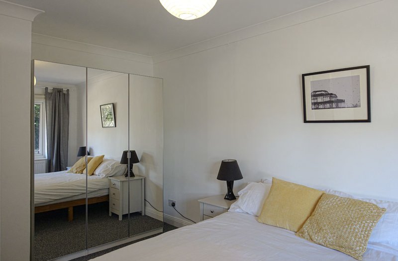 Bright bedroom with double bed, mirrored wardrobe, yellow cushions and bedside lamp