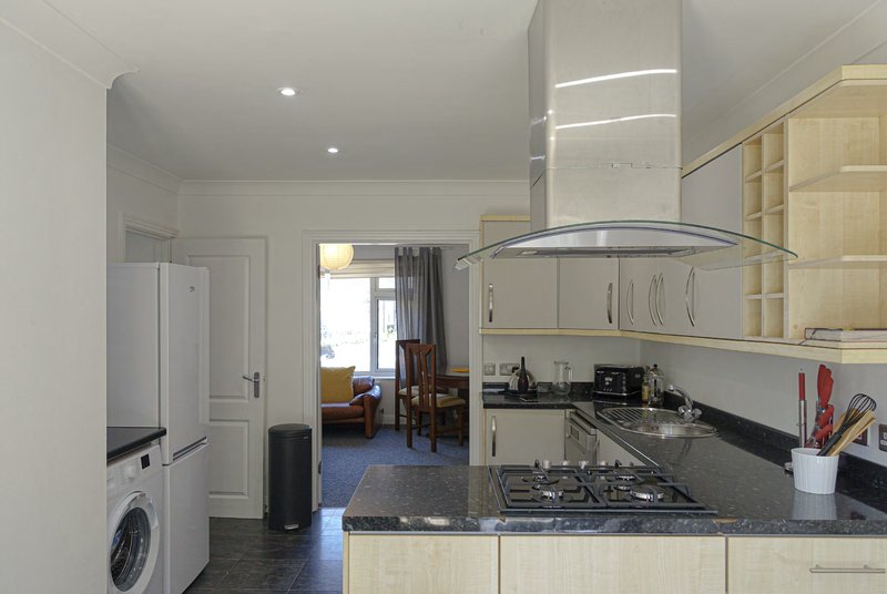 Open-plan kitchen and living area with cream cabinets, black countertop, gas range and stainless steel hood