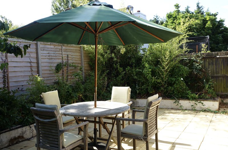 Garden patio with dining table, chairs, green umbrella and wooden fencing