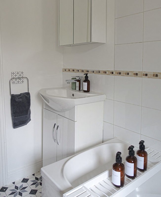 Clean bathroom with white sink vanity, mirror cabinet, bathtub and decorative toiletry bottles