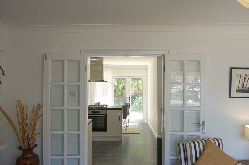 Open-plan living and kitchen area with white doors, striped cushions, and natural light from garden doors