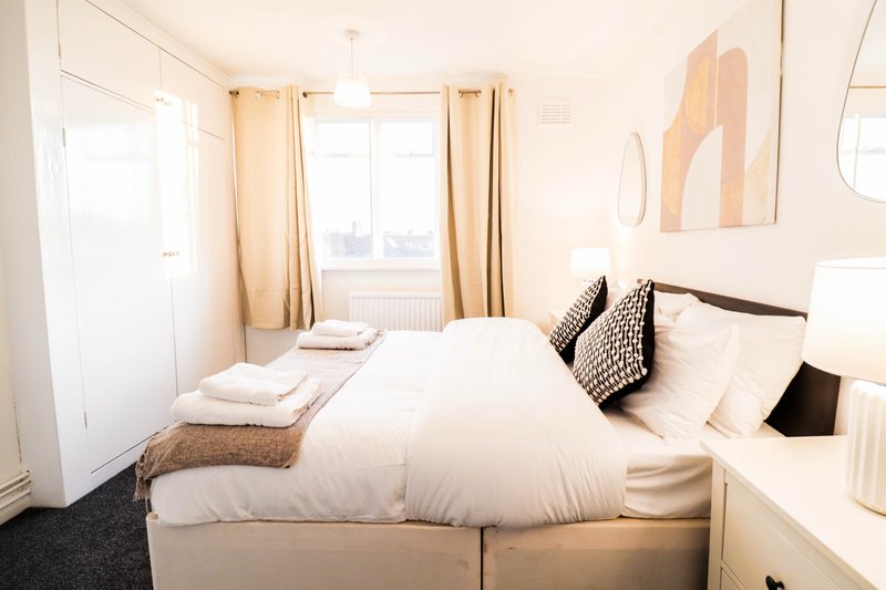 Bright bedroom with double bed, white bedding, cream curtains and modern wall art
