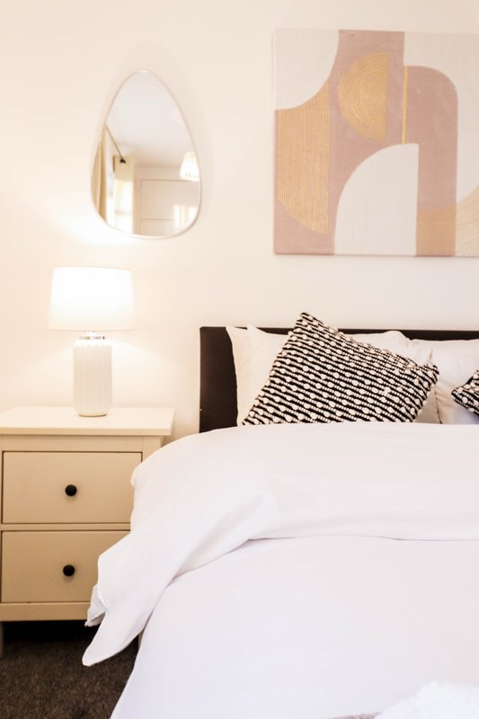 Bedroom with double bed, wooden nightstand, white lamp, and wall art