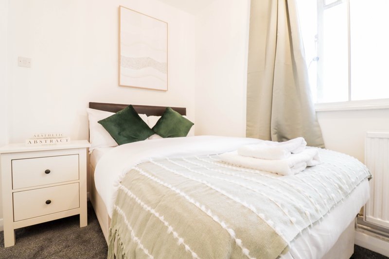 Bright bedroom with double bed, green cushions, wooden nightstand and window with curtains