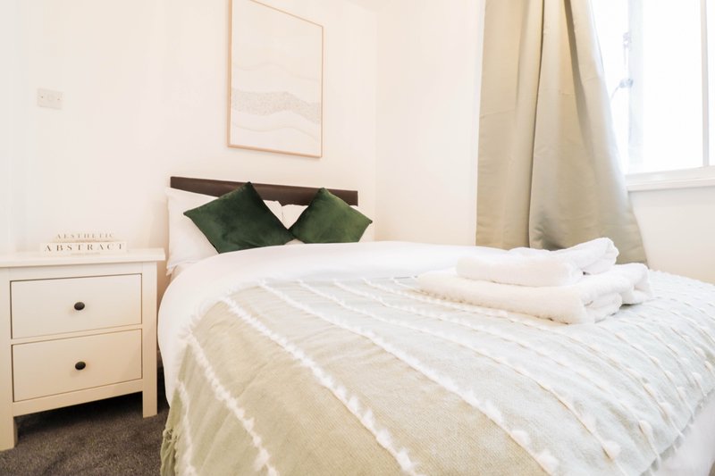 Bright bedroom with double bed, white bedding, cream curtains and wooden nightstand