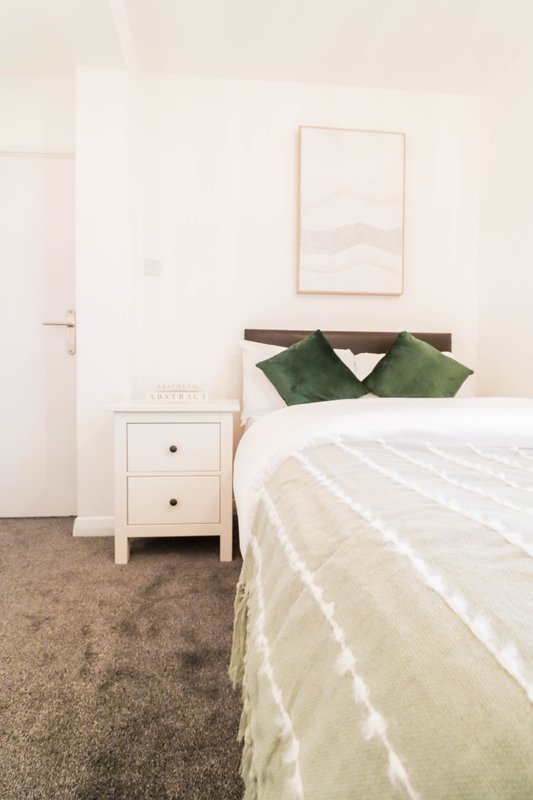 Bright bedroom with white bed, green cushions, white bedside table and framed wall art